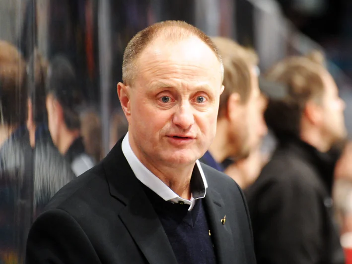 Anders Eldebrink i mörk kavaj vid spelarbåset under en hockeymatch, under tiden som tränare