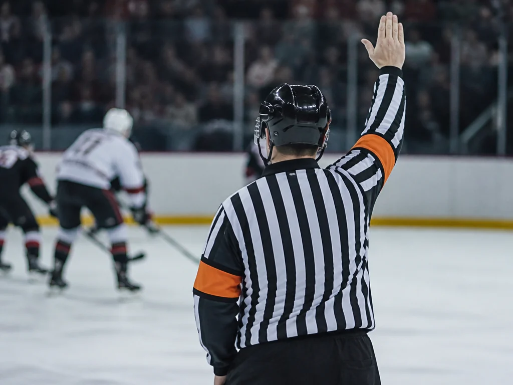 Ishockeydomare i randig domartröja visar en signal under match