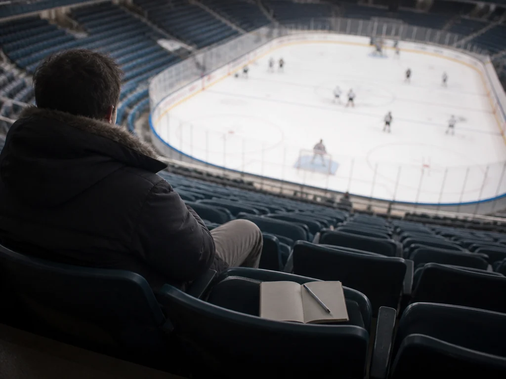 Scout med anteckningsblock följer en hockeymatch från läktaren